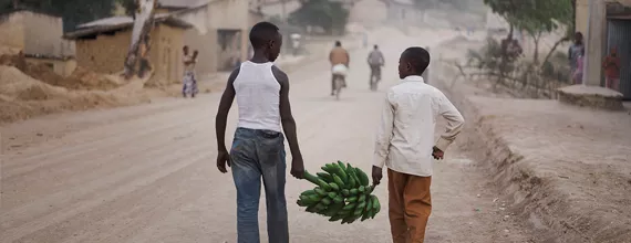 2 Jungen tragen eine Bananenstaude in einer Strasse in Ruanda