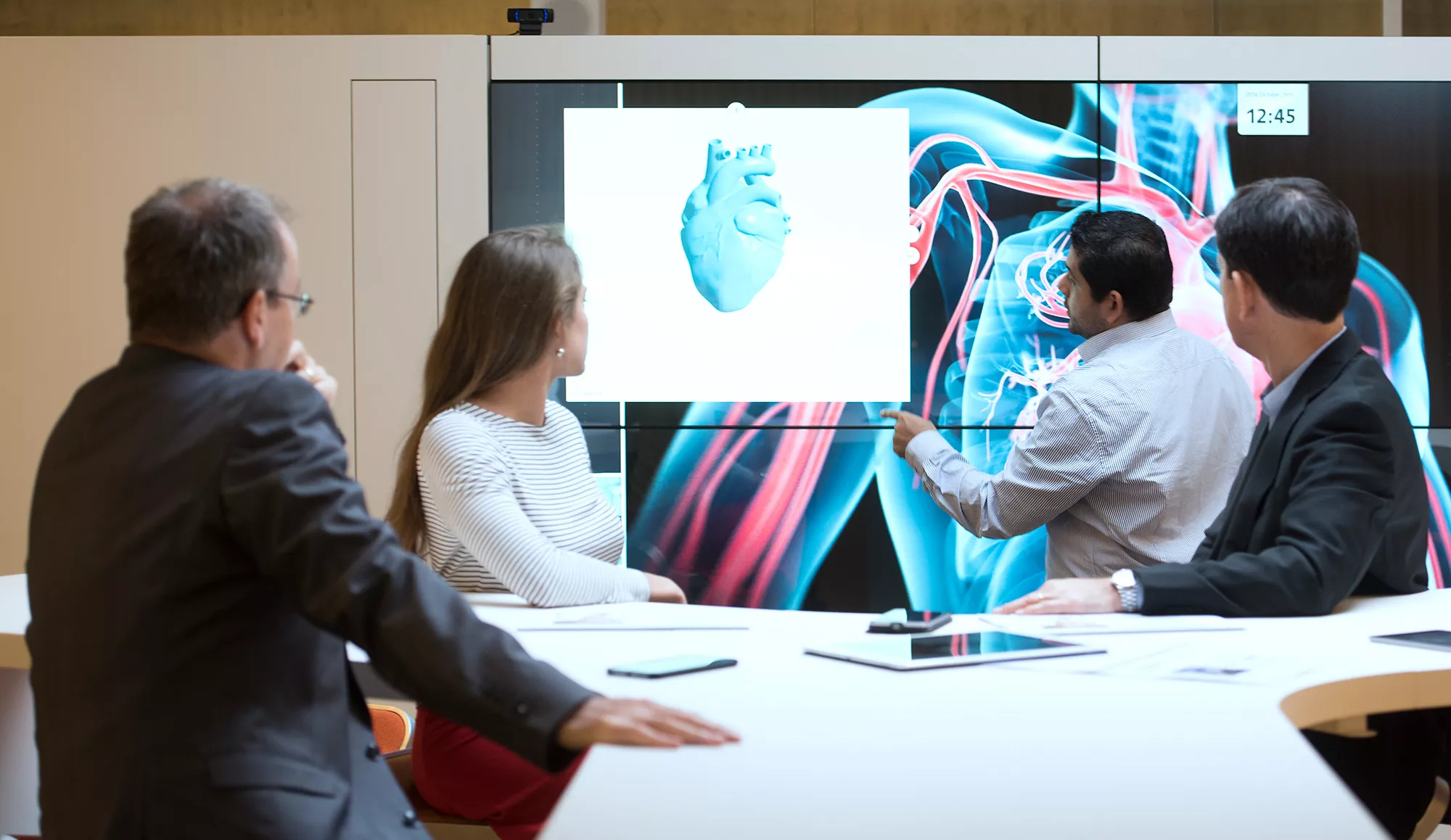 Business people in a meeting room looking at a screen displaying a 3D heart