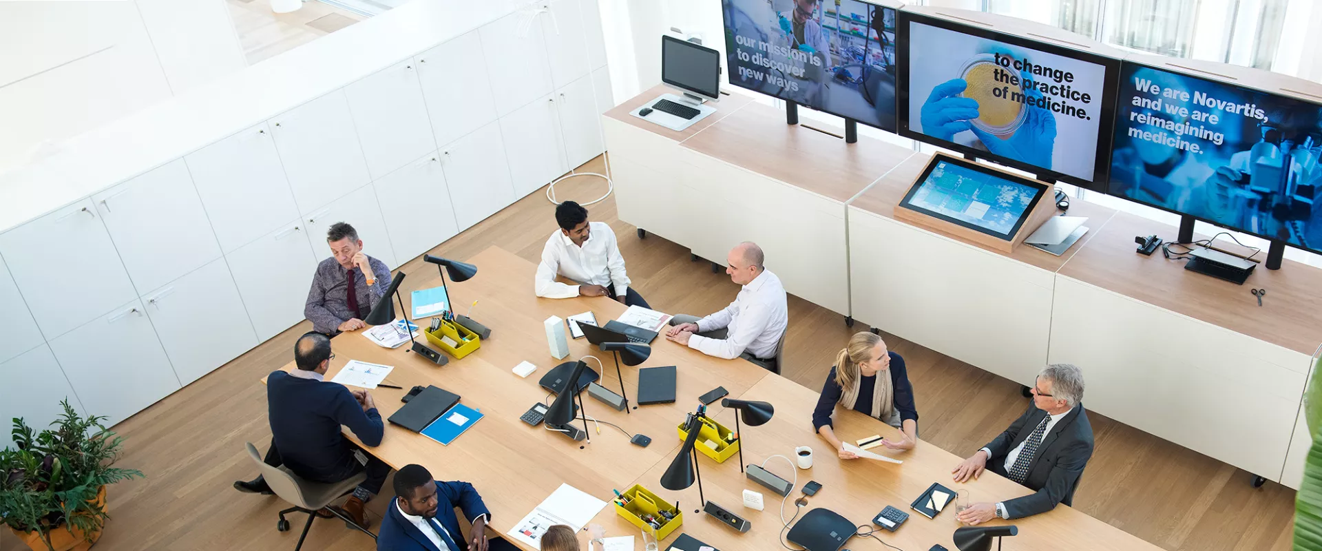 Overhead view of a meeting room with people in the foreground and screens in the background